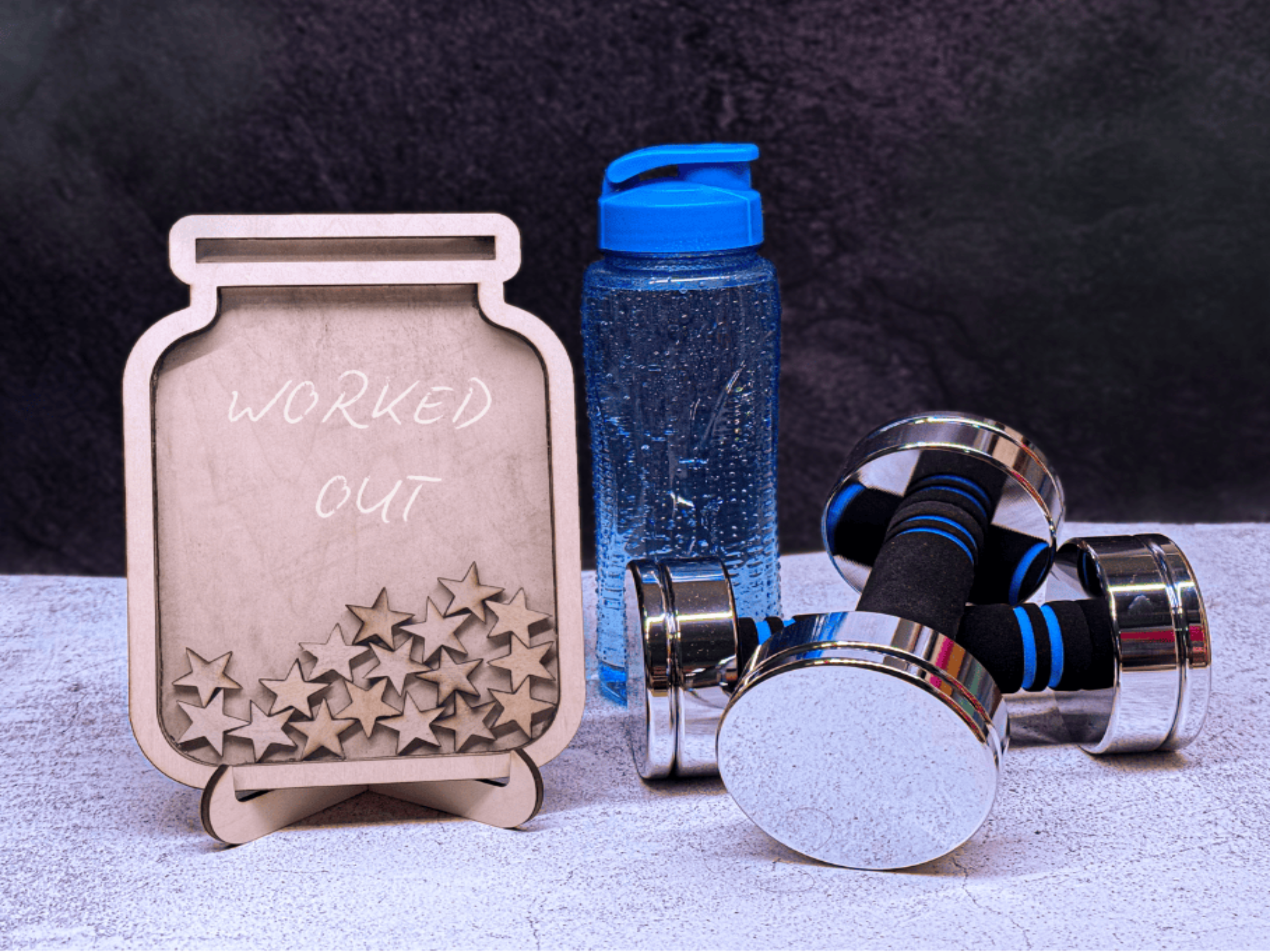 Dumbbells, water bottle, and motivational plaque on a textured surface with dark background